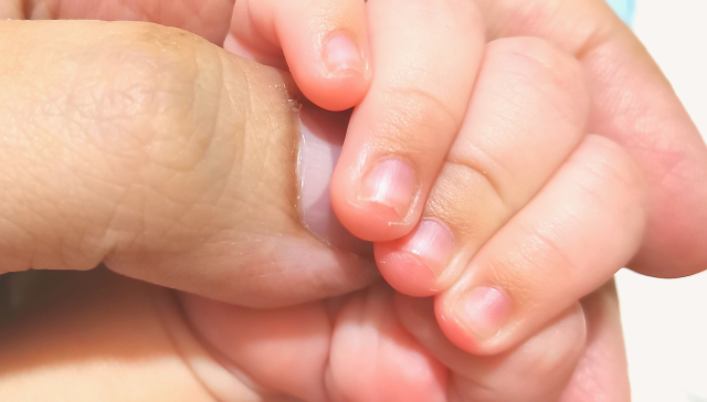 A mother holding the hand of her rainbow baby