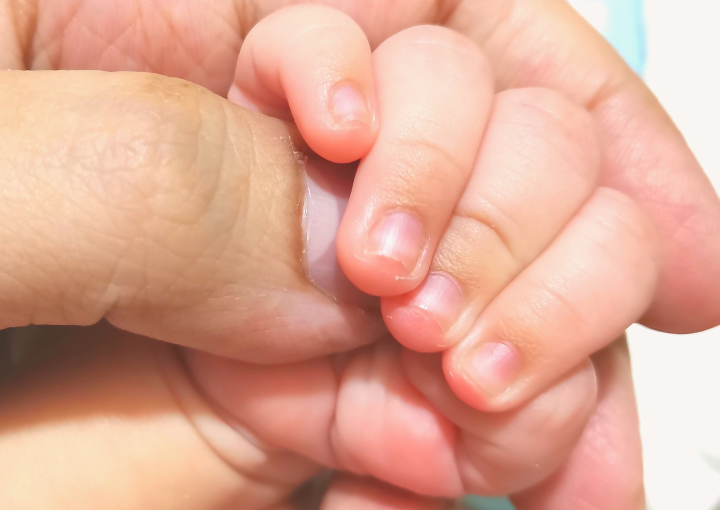 A mother holding the hand of her rainbow baby