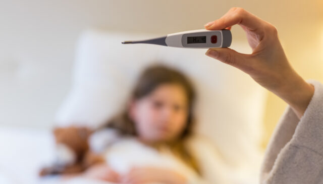 Mother checking body temperature on thermometer in bedroom