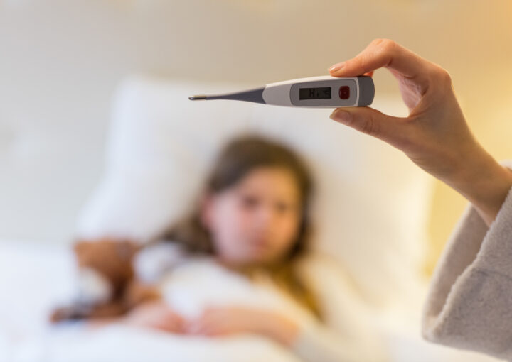 Mother checking body temperature on thermometer in bedroom